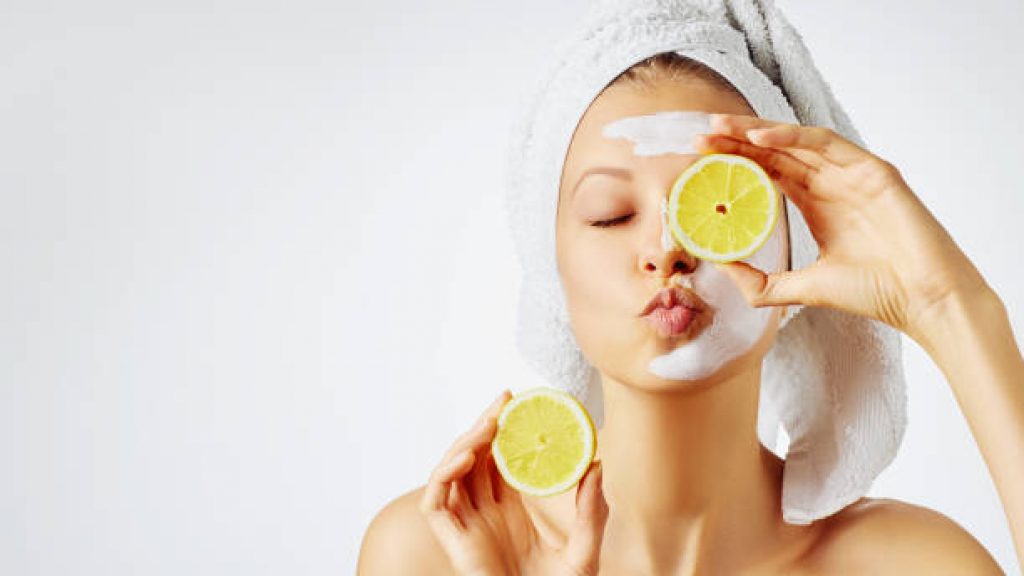 Woman with facial mask holds lemons, over white background with copy space